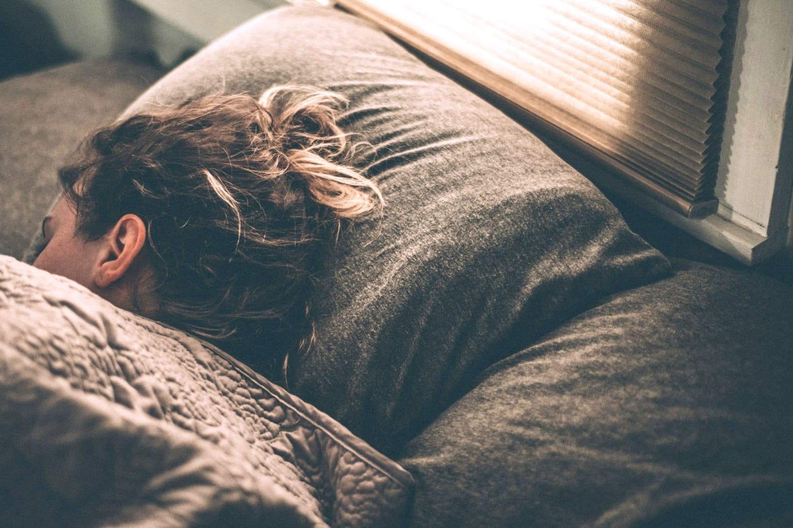 Femme endormie dans la lumière d’un store : le sommeil, pilier suivi par une napsothérapeute à Lyon.